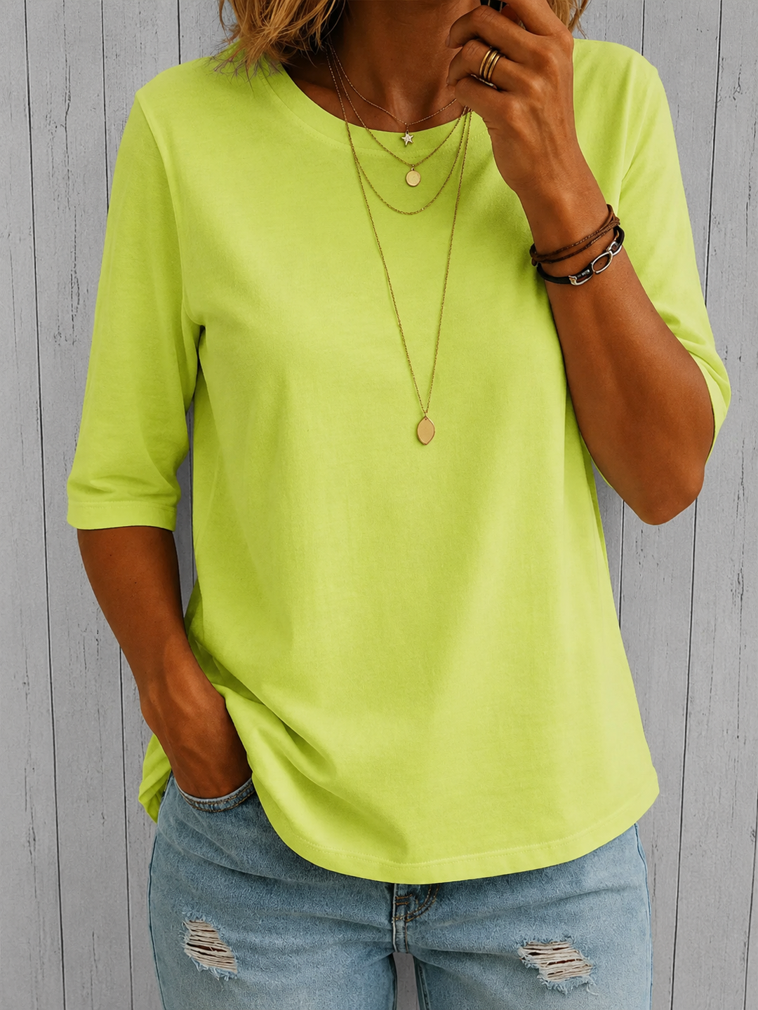 T-shirt vert anis vif à demi-manches porté par un mannequin avec un jean troué, devant un mur de lattes grises. 6