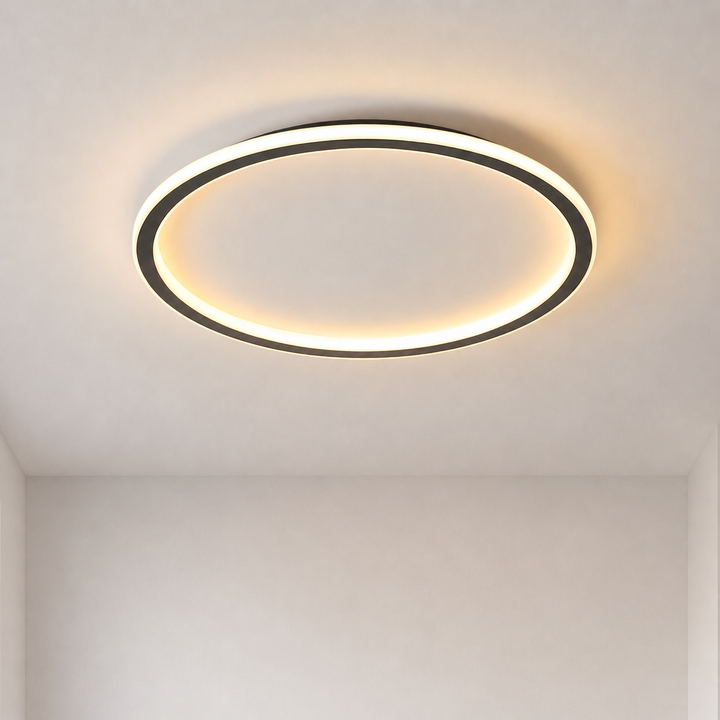 Plafonnier en anneau noir allumé, lumière chaude diffuse, vu de face sur un plafond clair dans une pièce vide. 1