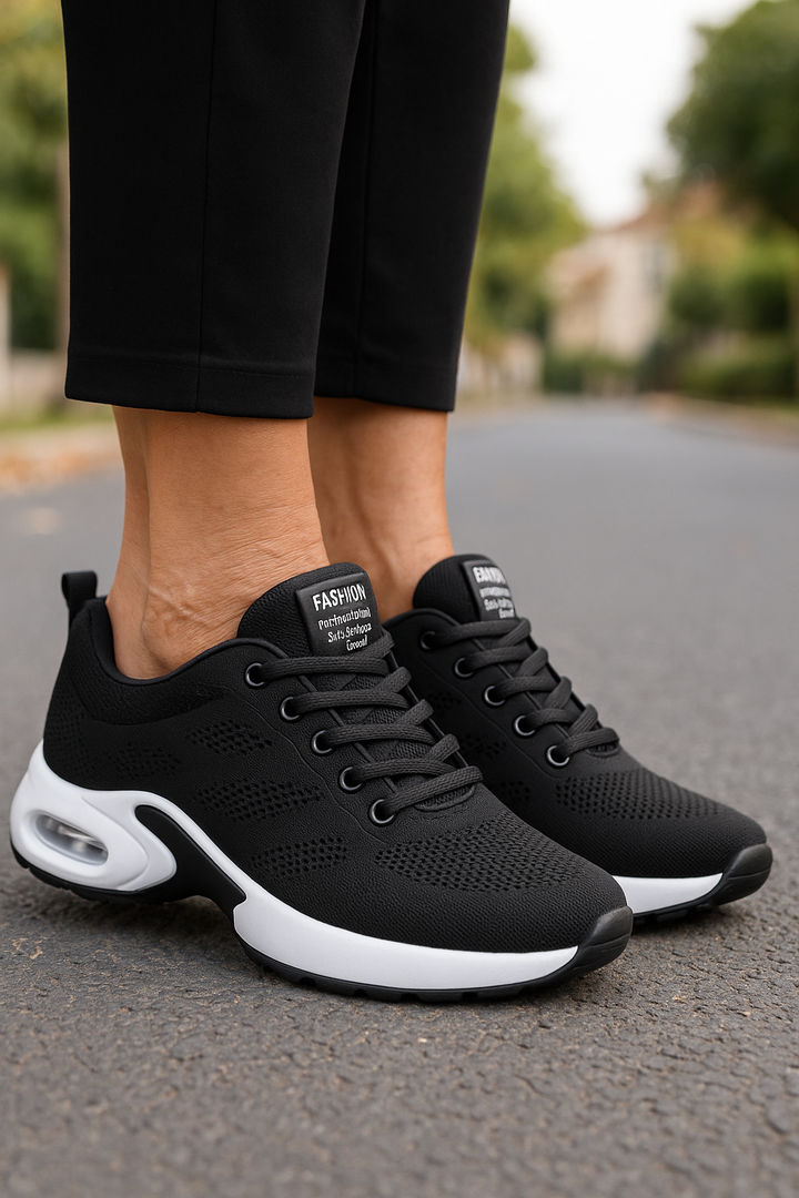 Paire de baskets noires en maille à semelle blanche et bulle d'air, portées avec un pantalon noir sur la chaussée. 6