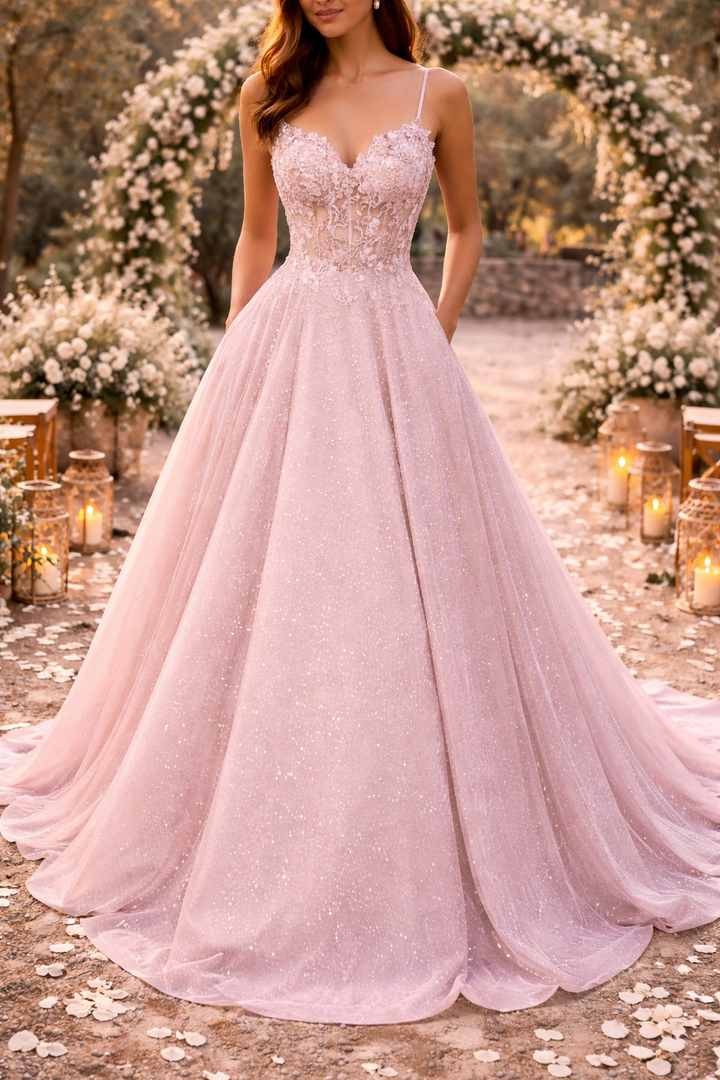Vue de face de la robe rose pâle portée par une mannequin, à fines bretelles et large jupe scintillante, devant une arche fleurie. 1