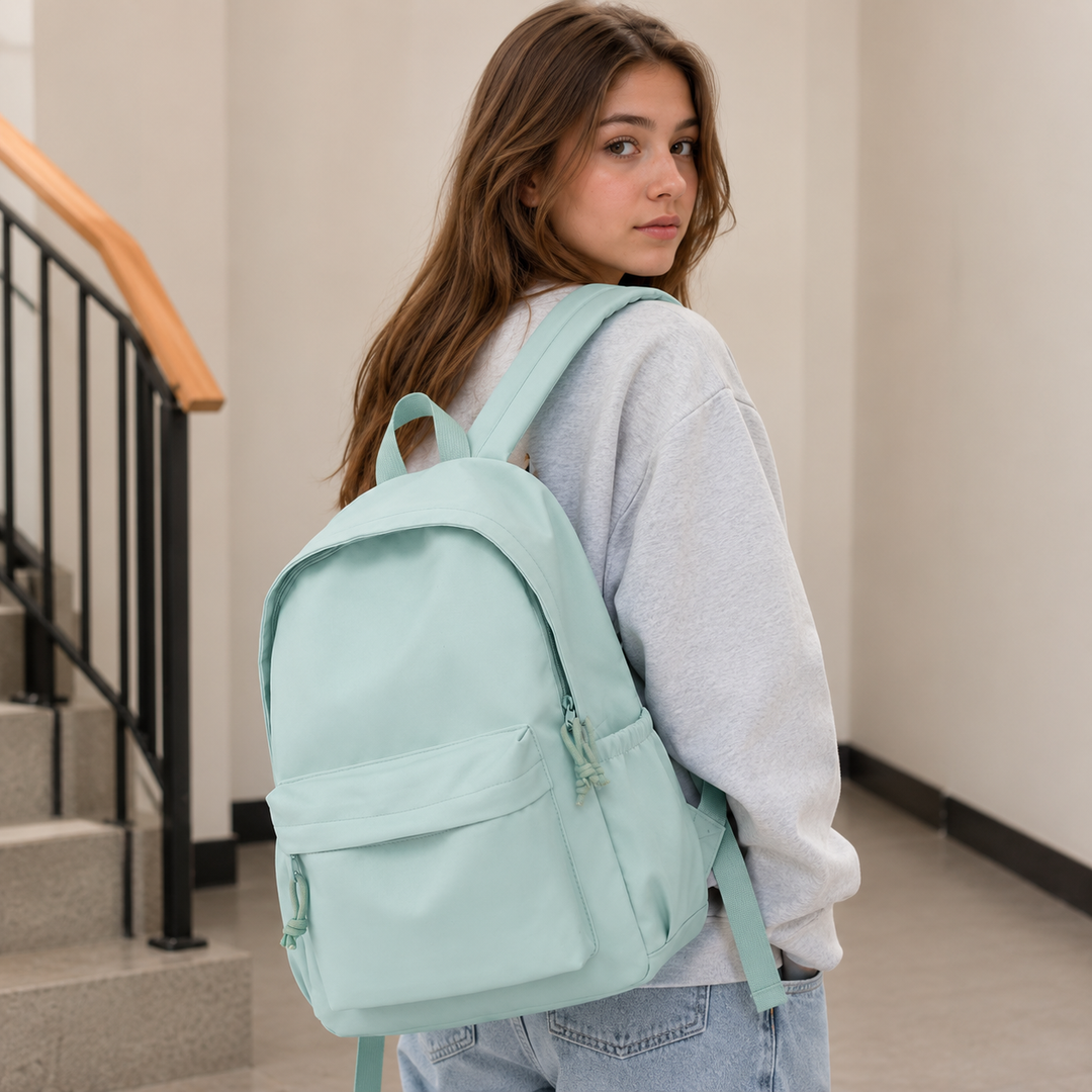 Jeune femme portant le sac à dos vert menthe sur une épaule, avec un sweat gris et un jean, dans un escalier. 3