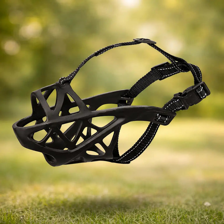 Muselière noire seule, vue de côté : panier souple ajouré, sangles à surpiqûres réfléchissantes et boucle à clip, sur fond d'herbe floue. 12
