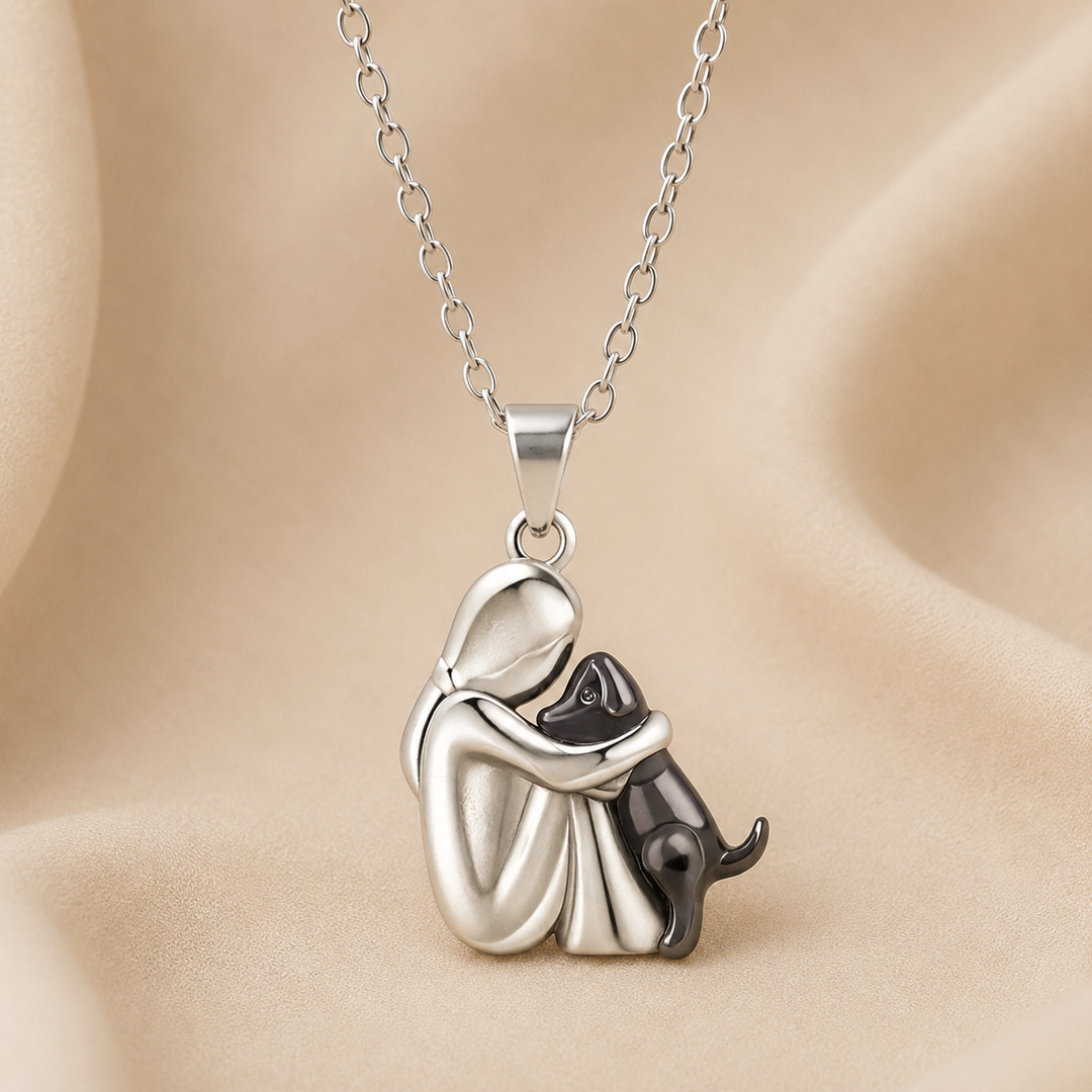 Pendentif d'une personne argentée mate étreignant un chien noir, vu de face sur un fond de tissu beige. 3