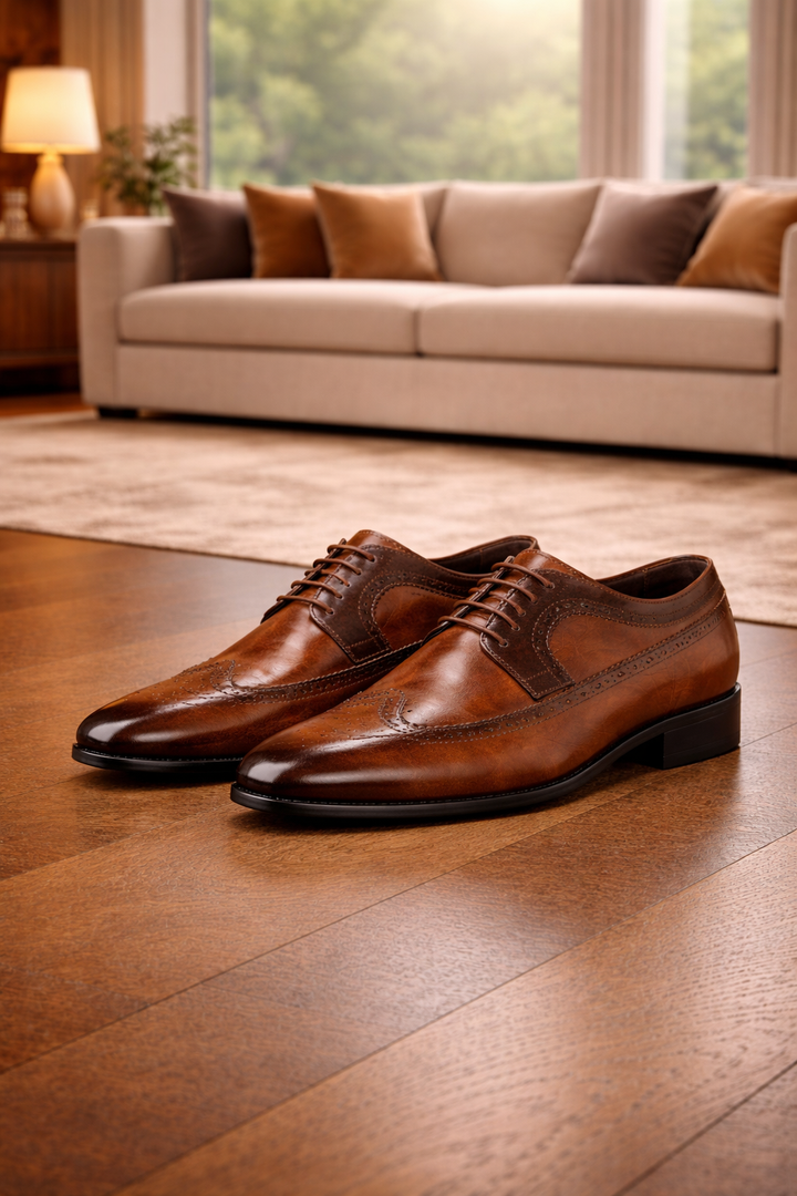 Paire de chaussures en cuir brun à lacets et motifs perforés posée sur un parquet devant un canapé beige. 3