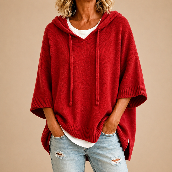 Poncho rouge en maille à capuche et manches trois-quarts, porté sur un t-shirt blanc et un jean clair déchiré. 10