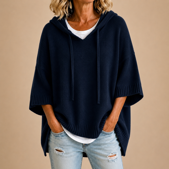 Poncho bleu marine en maille à capuche et cordons, porté sur un t-shirt blanc avec un jean clair déchiré. 7