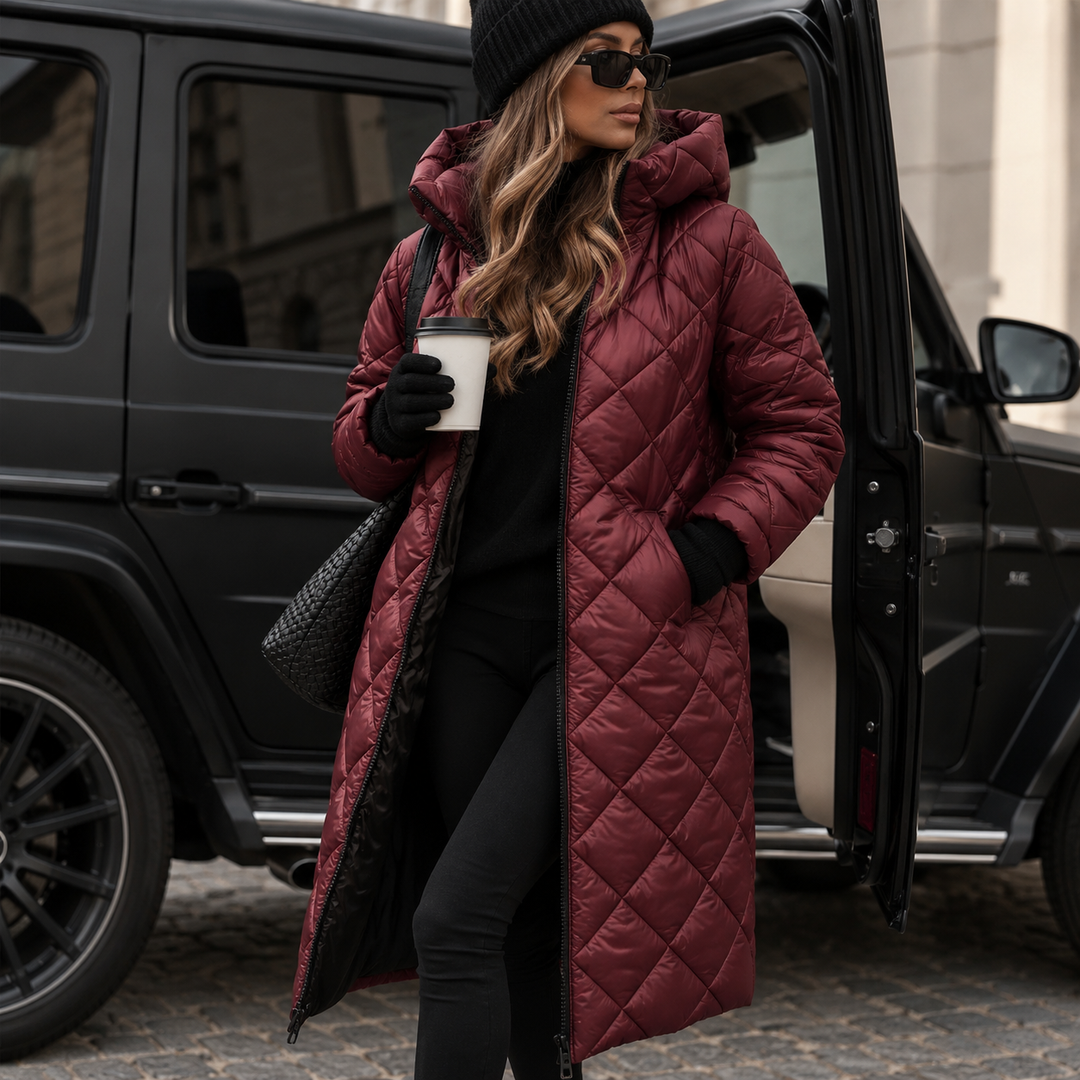 Femme portant le manteau long matelassé à capuche bordeaux brillant, zip ouvert, main dans la poche, tenue noire et sac tressé, devant un véhicule noir. 5