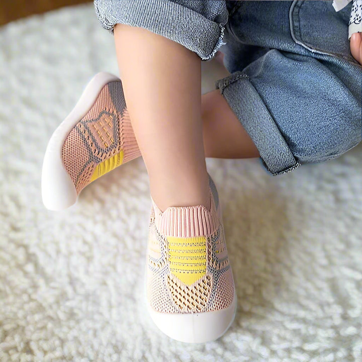 Jambes croisées d'un enfant sur un tapis blanc, chaussé de chaussures en maille rose à empiècement jaune, l'une montrant sa semelle. 13