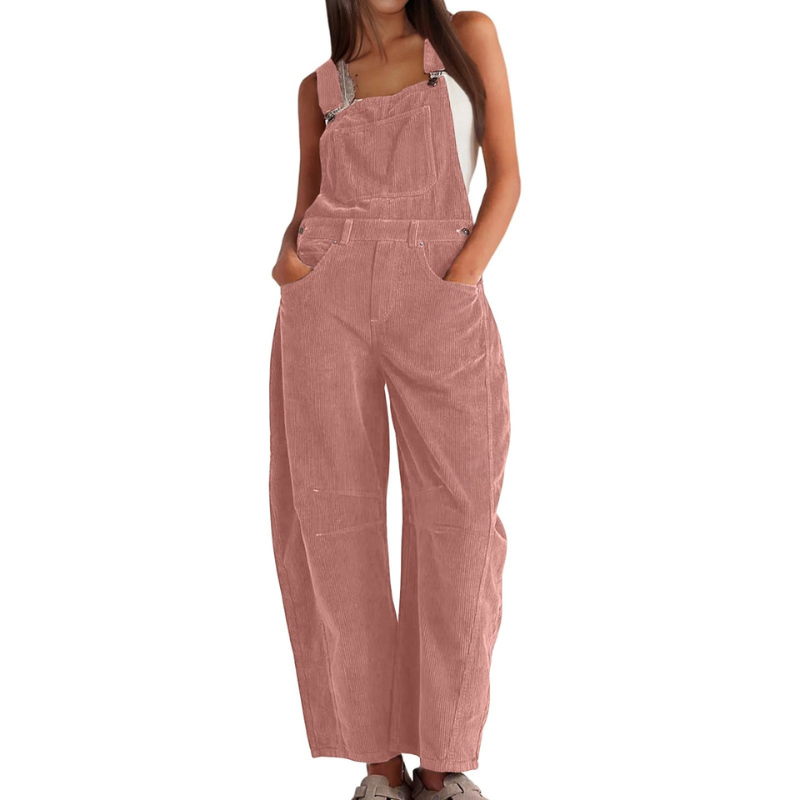Salopette en velours côtelé rose poudré portée de face par une femme, mains dans les poches, jambes larges et bretelles réglables. 1