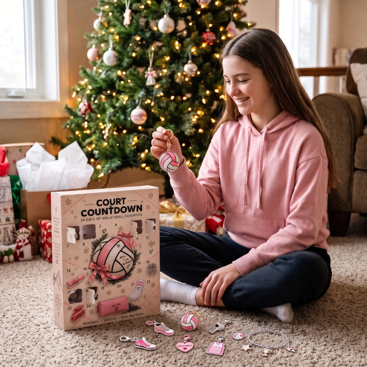 Adolescente en sweat rose assise devant un sapin de Noël, tenant un charm ballon de volley, boîte du calendrier à côté 1