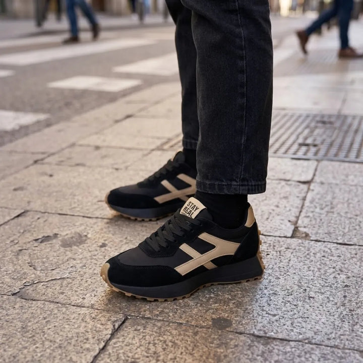 Baskets noires à bandes beiges portées avec un jean noir sur une chaussée dallée 17