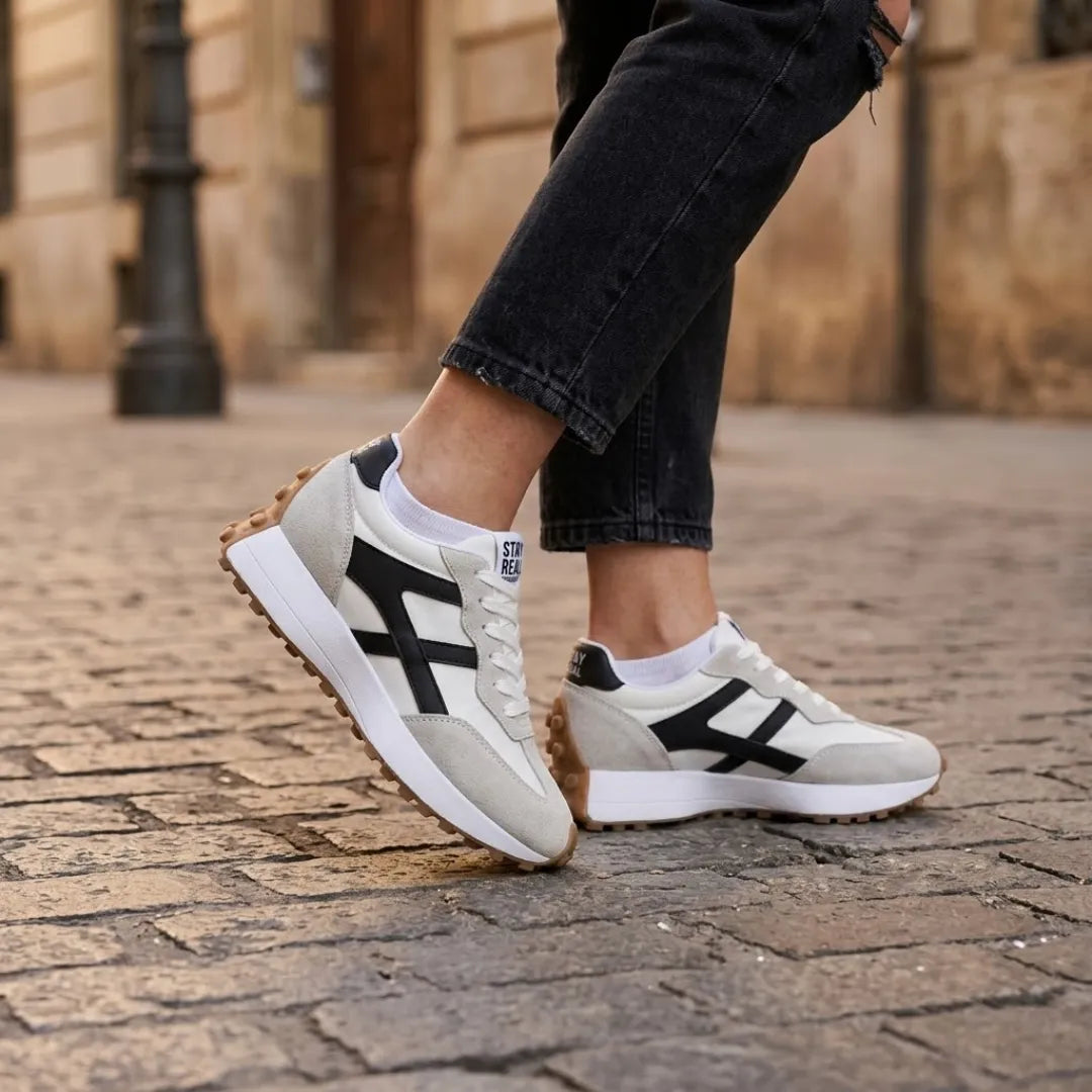 Baskets portées par une femme en jean noir et chaussettes blanches, sur des pavés 22