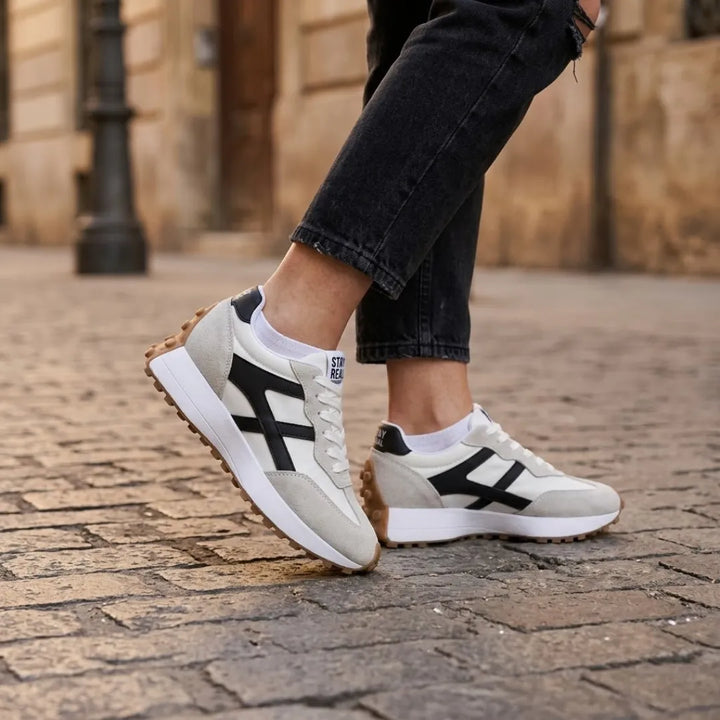 Baskets portées par une femme en jean noir et chaussettes blanches, sur des pavés 22