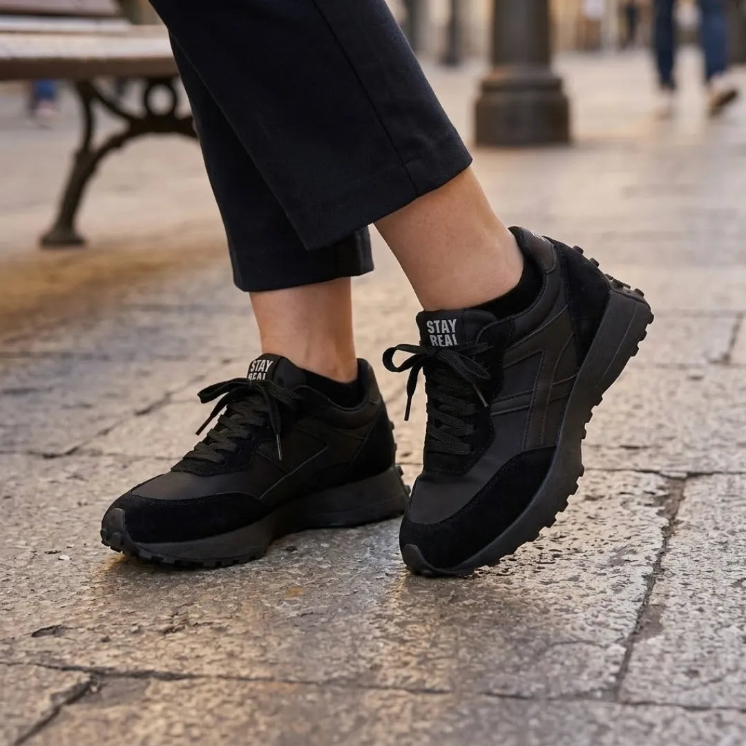 Baskets noires portées avec un pantalon noir, sur un sol dallé en ville 7
