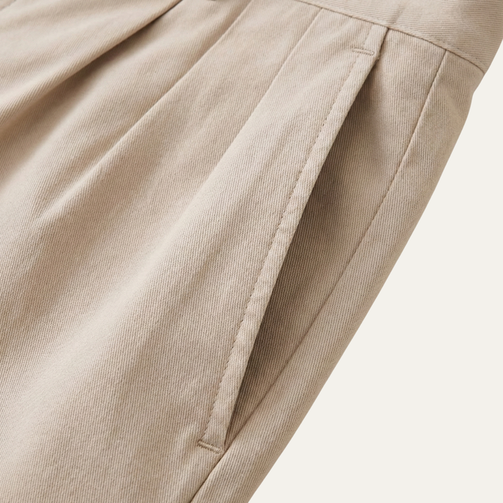 Détail de la poche latérale surpiquée et du pli à la taille du short beige, tissu en sergé. 4