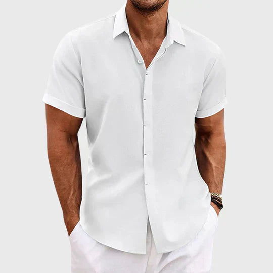 Chemise blanche à manches courtes retroussées, portée par un homme avec pantalon blanc, vue de face sur fond gris clair. 2