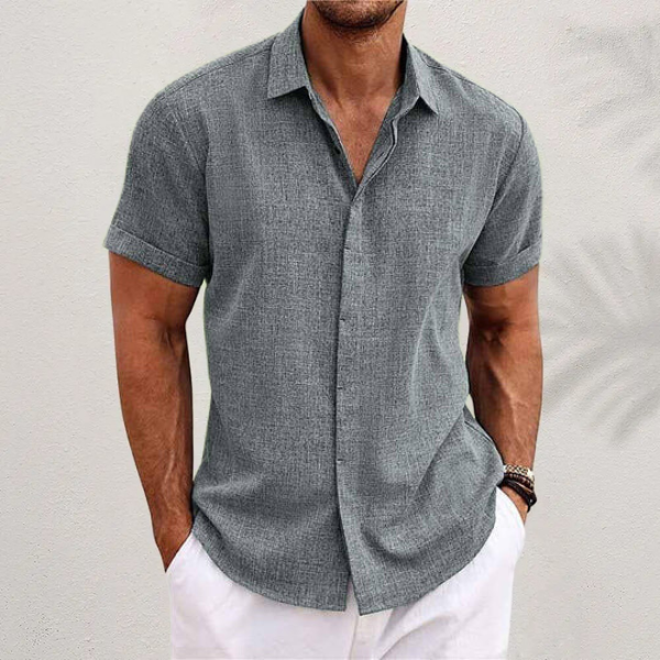 Chemise grise à tissage texturé, portée par un homme en pantalon blanc, manches retroussées, devant un mur clair. 3