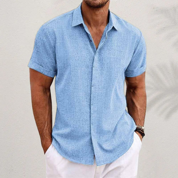 Chemise bleu ciel au tissu texturé, portée par un homme en pantalon blanc, avec bracelets au poignet, devant un mur clair. 5