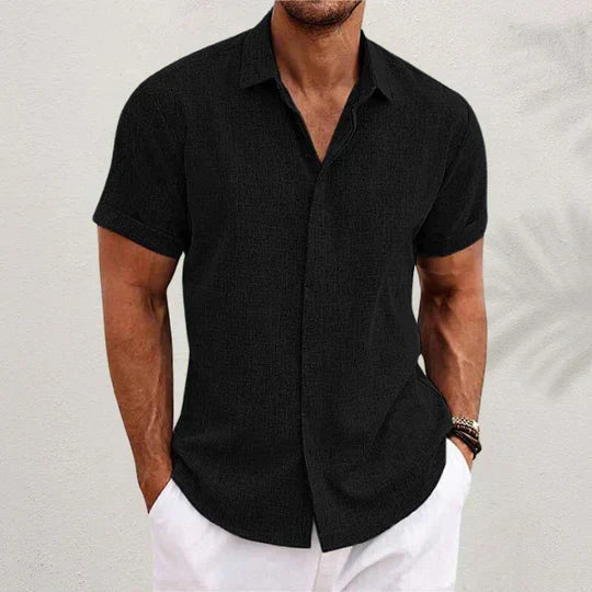 Chemise noire à fines rayures texturées, portée par un homme avec pantalon blanc, face, une main dans la poche. 1