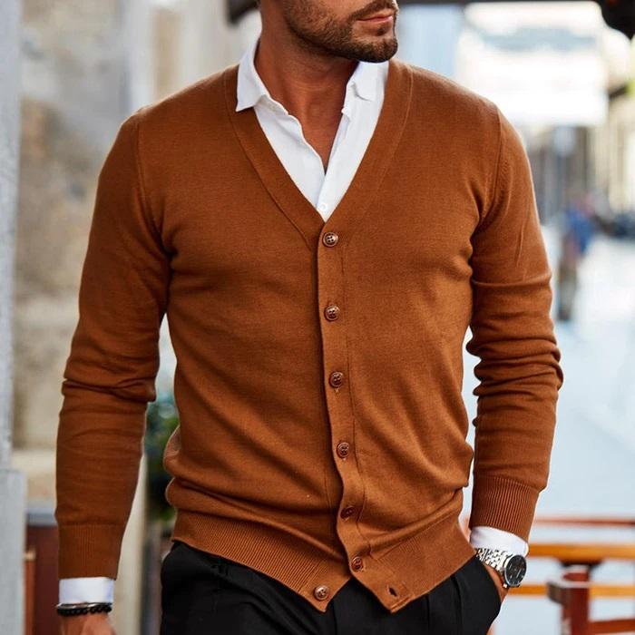 Cardigan marron caramel à boutons, porté par un homme en marche sur une chemise blanche et un pantalon noir. 2