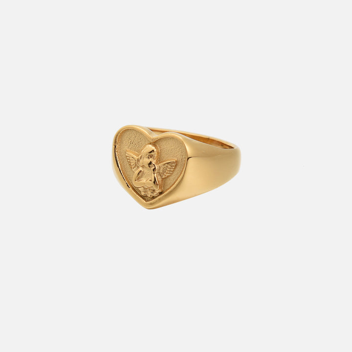 Bague chevalière dorée en forme de cœur ornée d'un petit ange ailé en relief, vue de trois quarts sur fond clair. 1