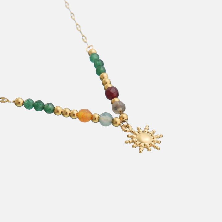 Collier doré posé en biais, gros plan sur les perles facettées colorées et le pendentif soleil 2