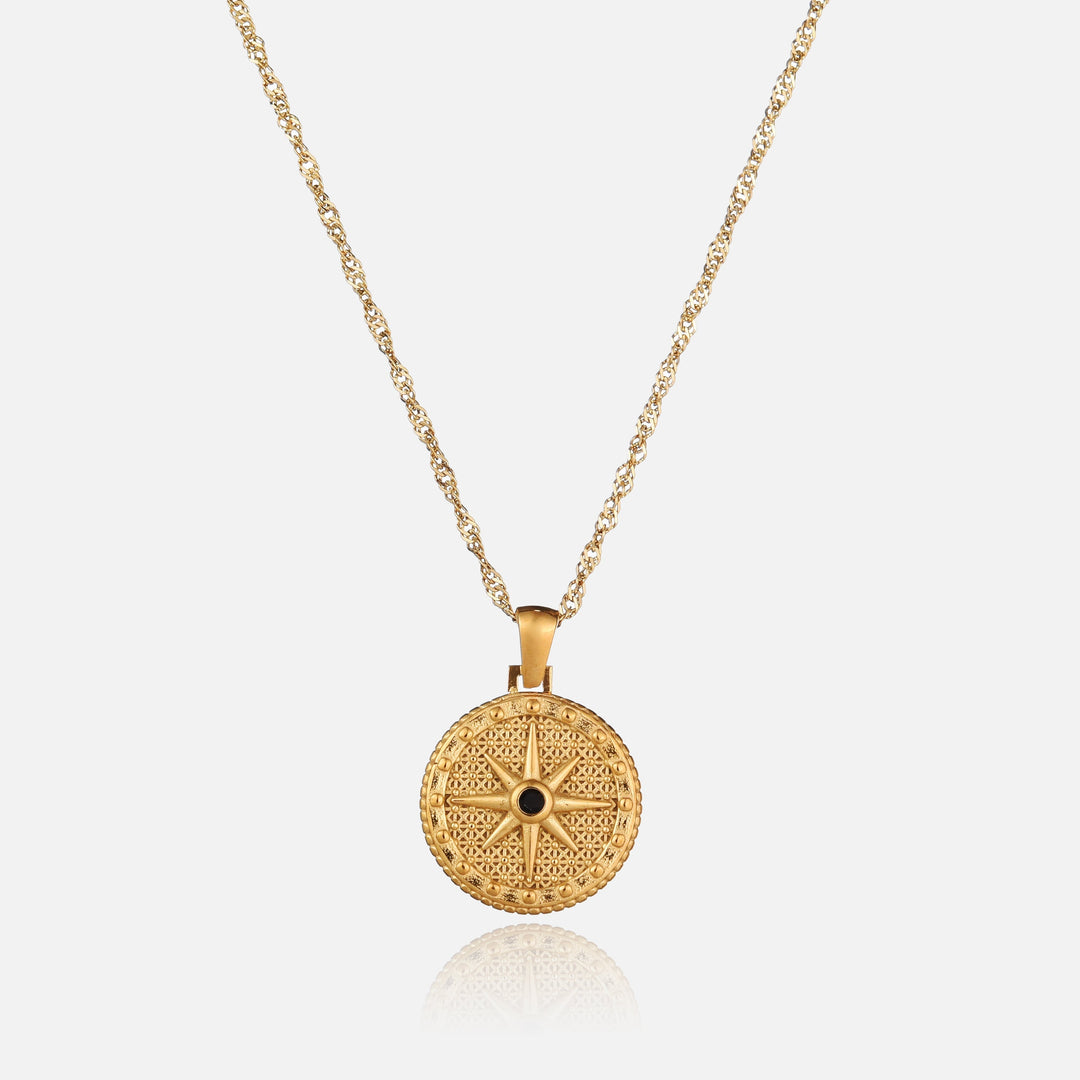Vue de face du pendentif rond doré orné d'une étoile à huit branches et d'une petite pierre noire, sur chaîne torsadée. 1