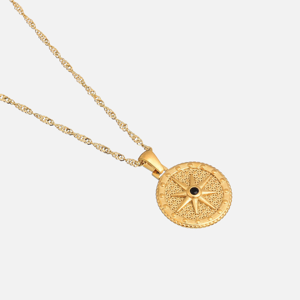 Pendentif rond en étoile avec pierre noire central, posé en biais sur sa chaîne torsadée dorée, fond clair. 2
