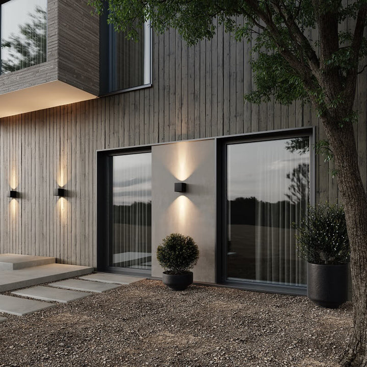 Appliques cubiques noires allumées en extérieur au crépuscule sur une façade en bois, éclairant le mur de haut en bas. 3