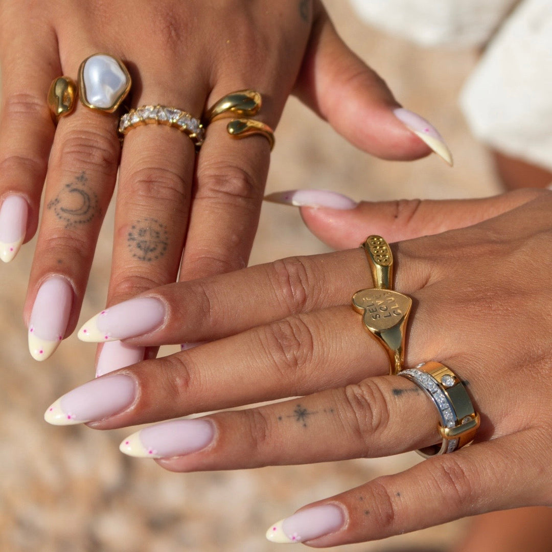 Deux mains aux ongles roses portant la bague au majeur avec plusieurs autres bagues dorées 4