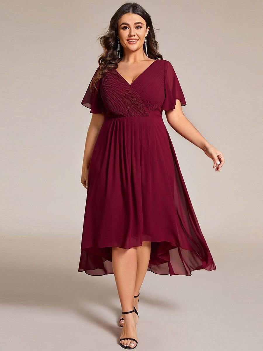 Robe bordeaux portée par un mannequin grande taille, corsage plissé en V, jupe fluide asymétrique, sandales noires, vue de face. 49