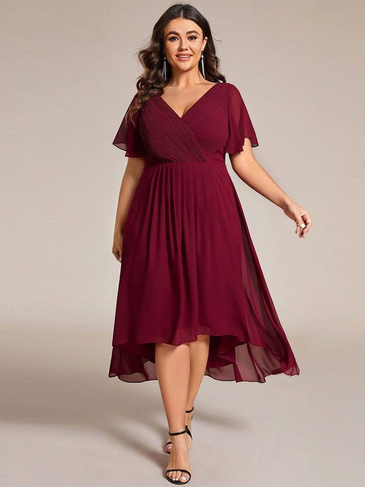 Robe bordeaux portée par un mannequin grande taille, corsage plissé en V, jupe fluide asymétrique, sandales noires, vue de face. 49