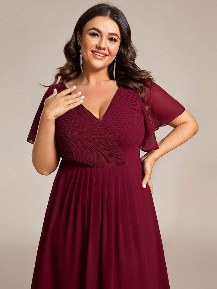 Gros plan sur le buste plissé et les manches papillon de la robe bordeaux, mannequin grande taille souriante avec boucles d'oreilles pendantes. 51