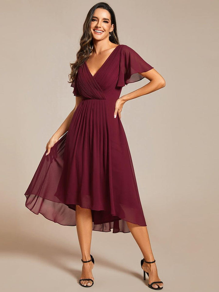 Mannequin en robe bordeaux, main sur la hanche, soulevant légèrement la jupe asymétrique transparente, vue de face. 48