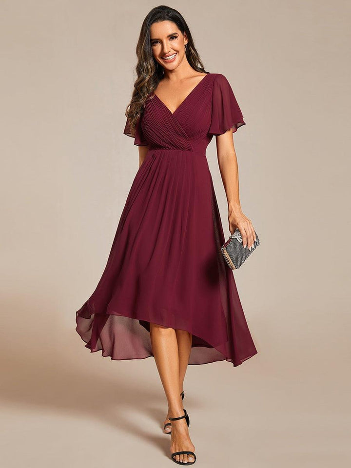 Robe bordeaux en mousseline portée de face, buste plissé croisé, ourlet asymétrique et petite pochette à la main. 3