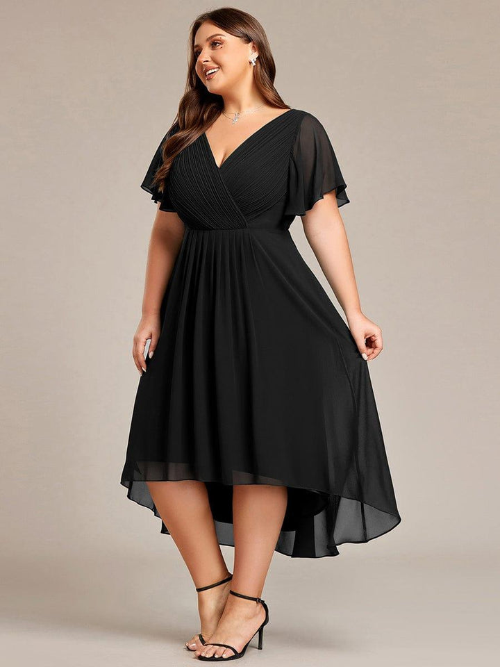 Robe noire grande taille vue de trois quarts, mannequin souriante, jupe plissée à ourlet asymétrique et sandales noires à brides. 29