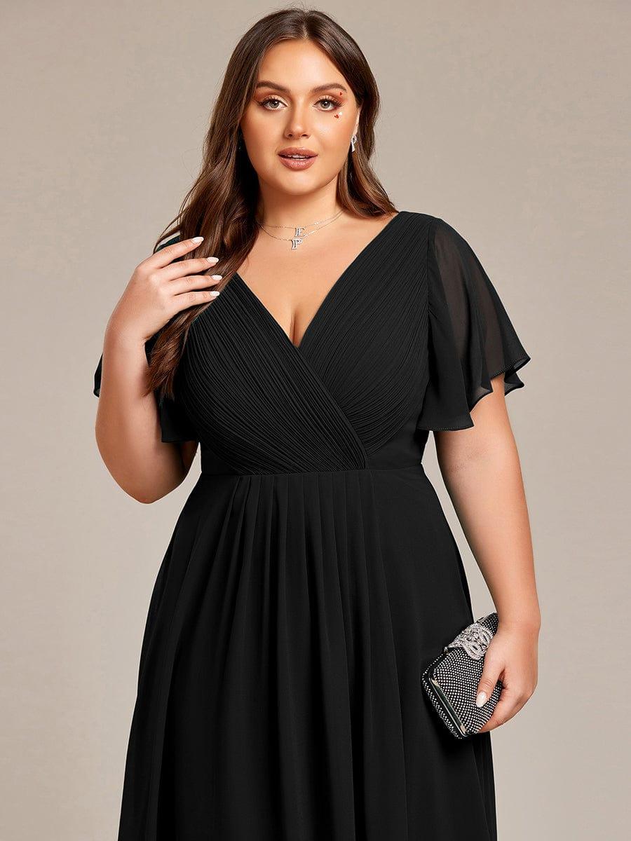 Gros plan sur le buste de la robe noire grande taille, corsage plissé croisé, manches volantées et pochette scintillante à la main. 28