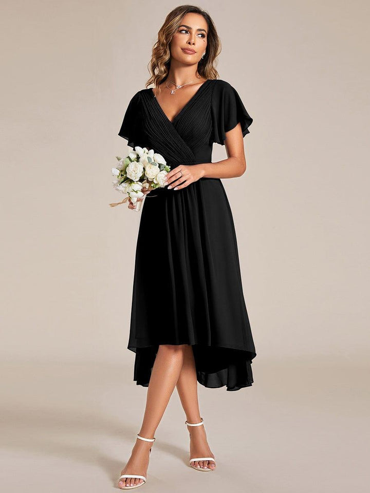 Robe noire portée par une mannequin tenant un bouquet de fleurs blanches, silhouette de face, jambes croisées, sandales blanches. 24