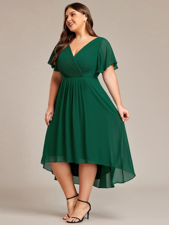 Robe vert foncé grande taille vue de trois quarts, mannequin souriante, jupe plissée à ourlet asymétrique et sandales noires. 39