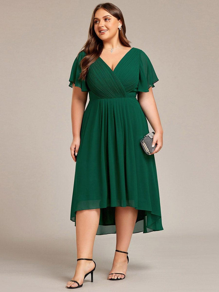 Robe vert foncé grande taille portée de face, mannequin tenant une pochette scintillante, ourlet plus long derrière. 40