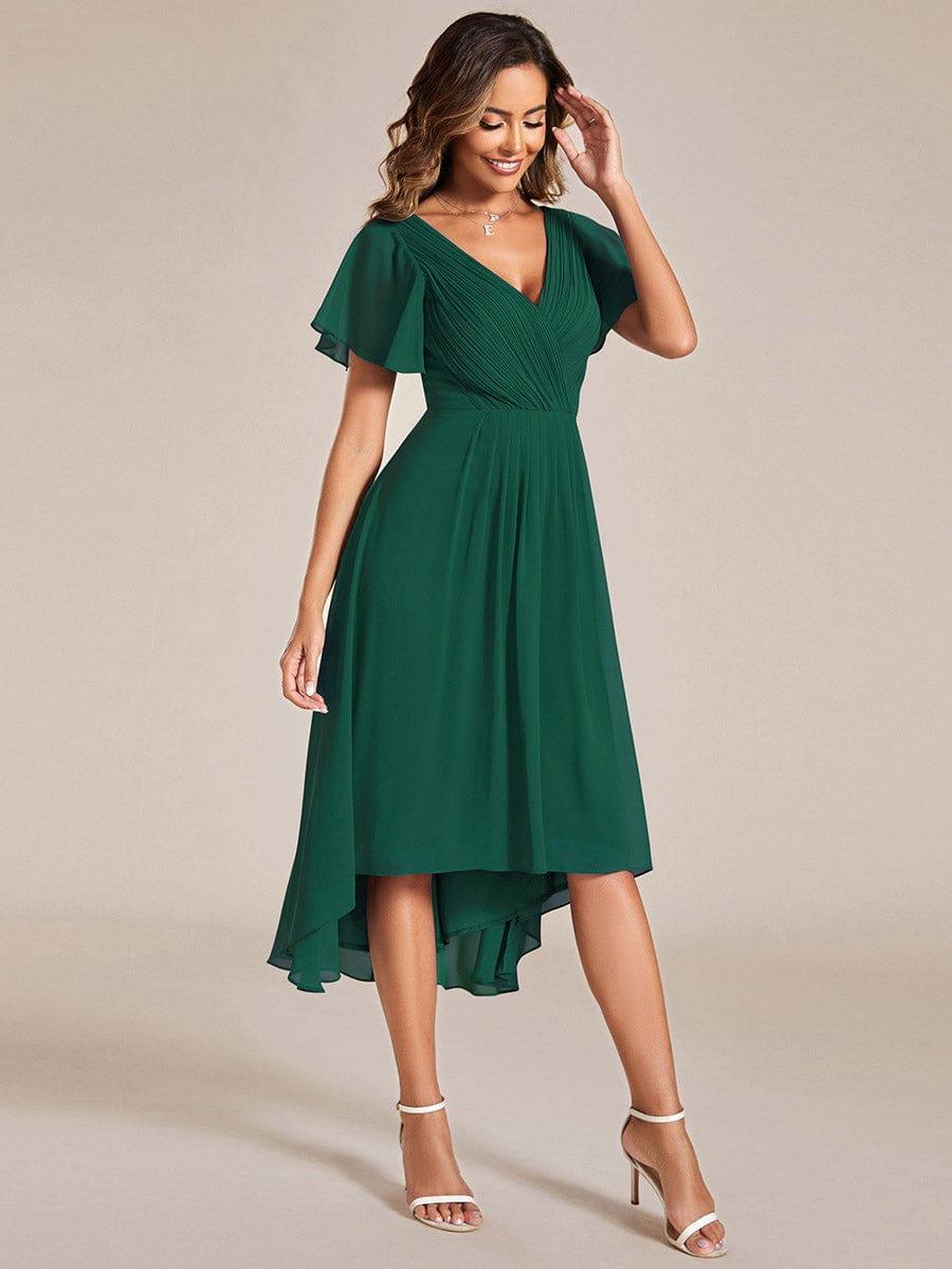 Robe vert foncé portée de trois quarts, mannequin souriante main près du visage, jupe fluide plus longue à gauche. 14