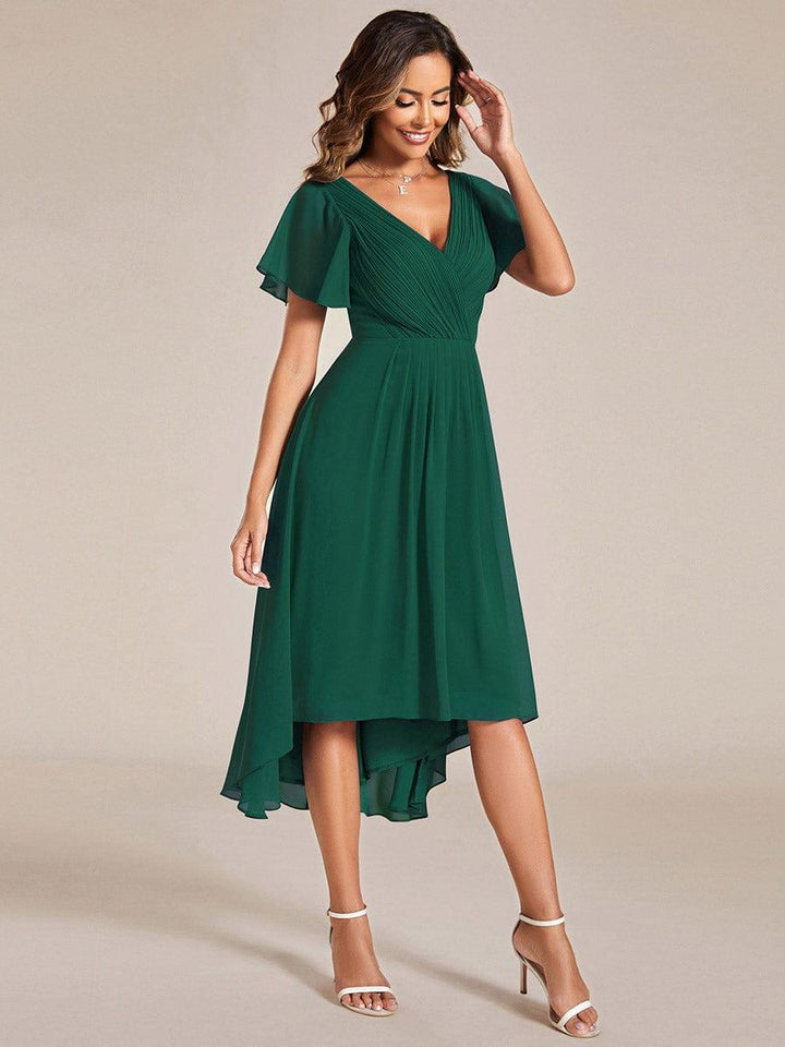 Robe vert foncé portée de trois quarts, mannequin souriante main près du visage, jupe fluide plus longue à gauche. 14