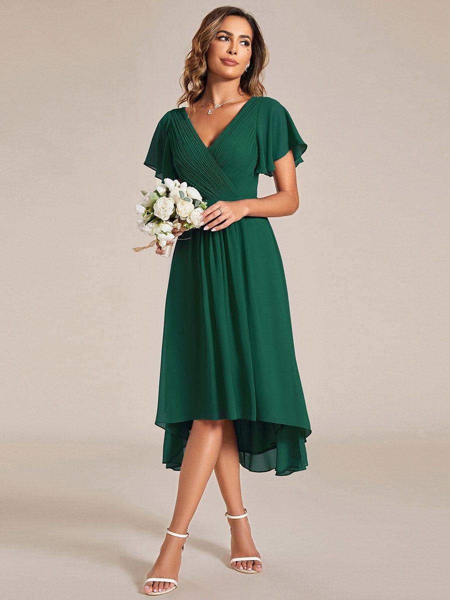 Robe vert foncé portée avec un bouquet de fleurs blanches, regard de côté, jupe en mousseline à ourlet asymétrique. 13