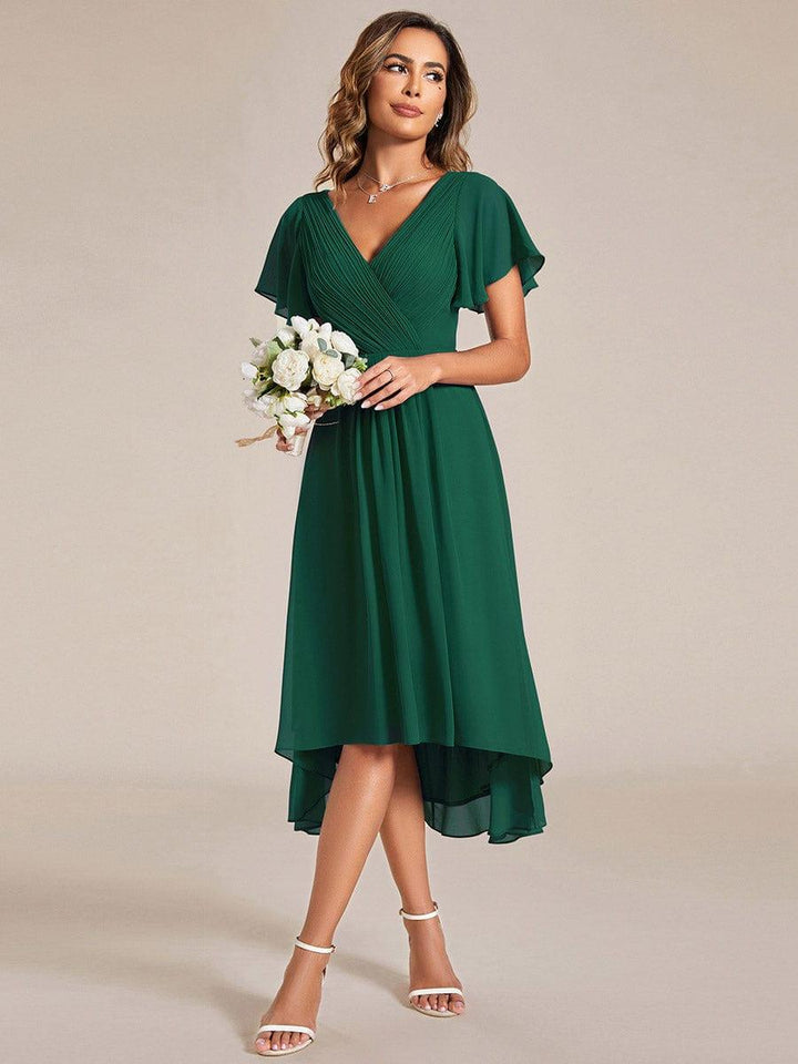Robe vert foncé portée avec un bouquet de fleurs blanches, regard de côté, jupe en mousseline à ourlet asymétrique. 13