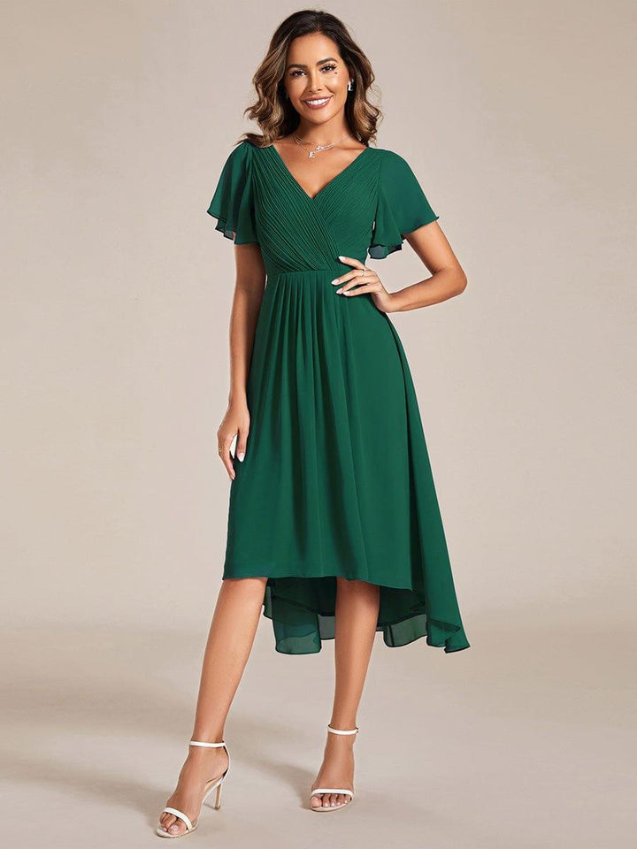 Robe vert foncé portée de face, main sur la hanche, buste plissé croisé, manches volantées et ourlet asymétrique. 10