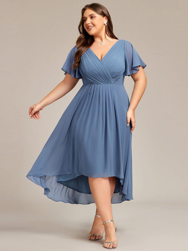 Robe bleu grisé portée par un mannequin grande taille, jupe asymétrique mi-longue, corsage plissé en V et manches papillon, vue de face en mouvement. 41