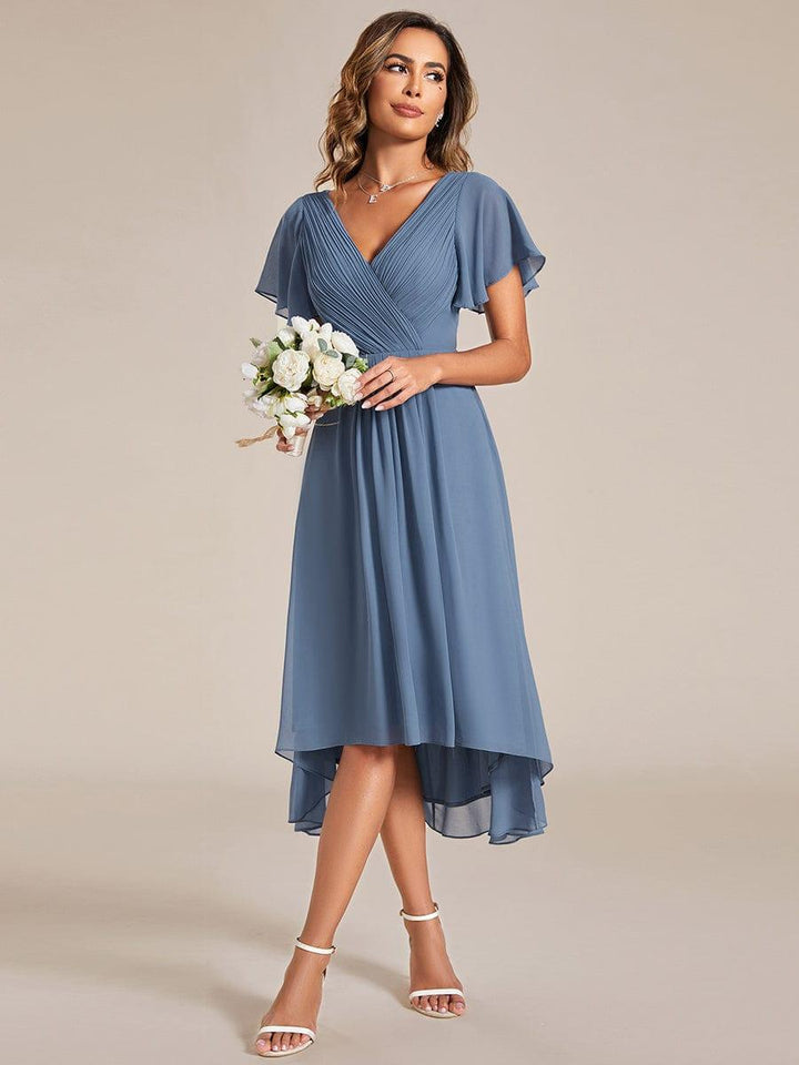 Robe bleu grisé portée avec un petit bouquet de fleurs blanches, silhouette de trois quarts, ourlet asymétrique. 8