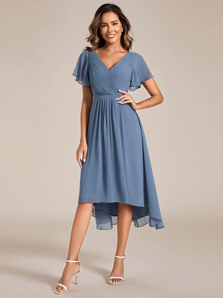 Robe bleu grisé portée de face, main sur la hanche, buste plissé, manches papillon et sandales blanches. 5
