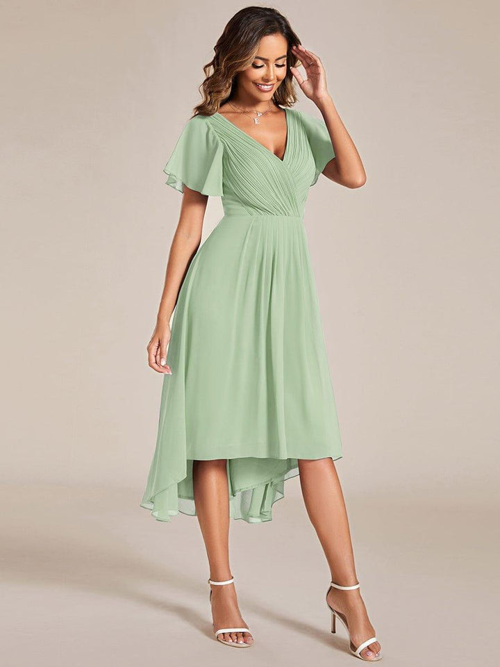 Robe vert sauge portée de trois quarts par une mannequin, une main près du visage, ourlet asymétrique et manches courtes volantées. 80