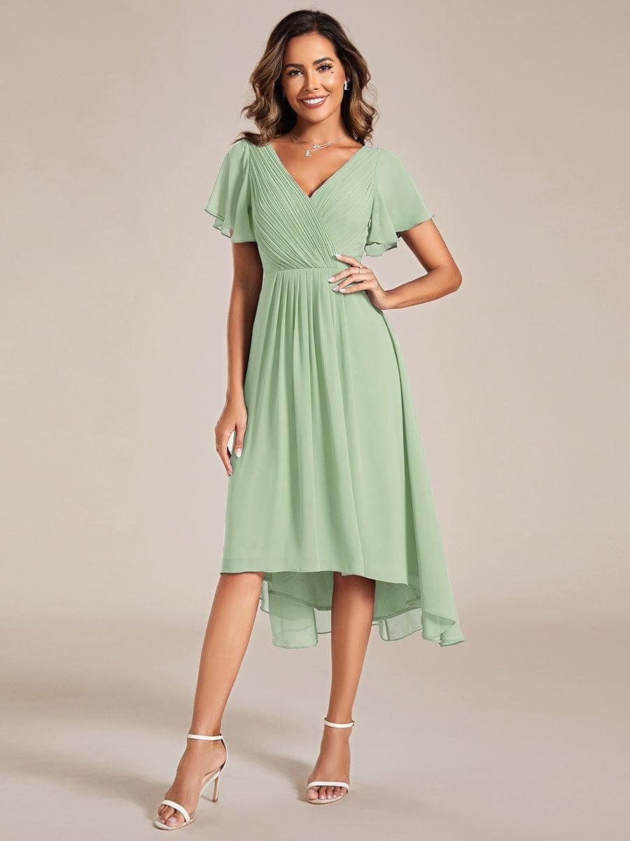 Robe vert sauge portée de face par une mannequin, main sur la hanche, col en V plissé et ourlet asymétrique. 76